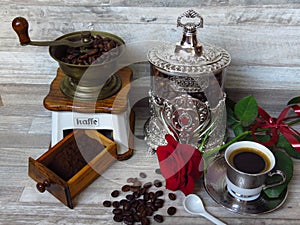 An old classic coffee grinder, silver coffee jar, a cup of coffee and a red rose. Retro style.