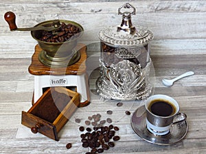 An old classic coffee grinder, silver coffee jar, a cup of coffee, porcelain spoon, coffee beans and minced coffee. Retro style.