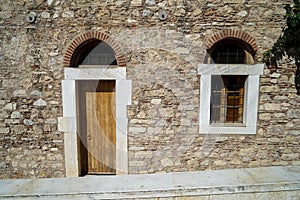 Old classic little church arch door and window frame on earth tone natural stone wall facade background with marble curb in front