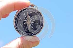 Old classic navigation compass in hand against blue sky background