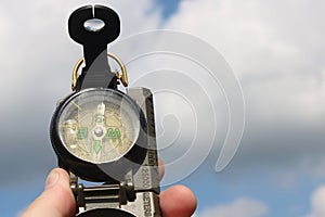 Old classic navigation compass in hand against blue sky background