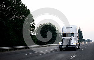 Old classic white high cab big rig power semi truck tractor driving by wide evening highway