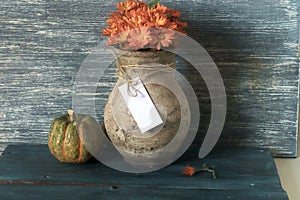 Old clay jug with a bouquet of flowers and pumpkins on a wooden table