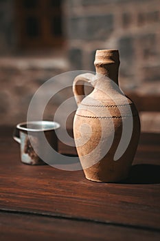 An old clay jug and with a glass stand on the wooden table.