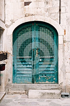 Old closed doors in green with bars on the windows in the oval doorway.