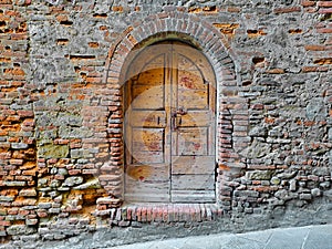 Old closed italian traditional wooden door against an old brick wall with arched opening