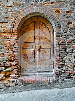 Old closed italian traditional wooden door against an old brick wall with arched opening