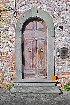 Old closed italian traditional wooden door against an old brick wall with arched opening