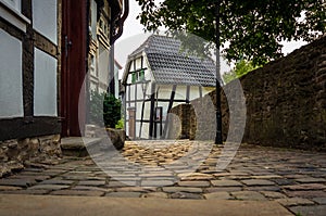 Old cobblestone alley, half-timbered houses on the left and a stone wall right on the edge of the picture, Hattingen