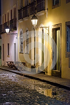 Old cobblestone street with lantern-lit colonial houses at night