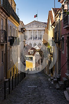 An old cobblestone street with traditional colorful buildings leading to the Portugese Parliament on the background, in the city o