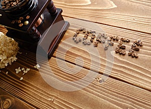 Old coffee mill and the word COFFEE written with coffee beans on a wooden surface