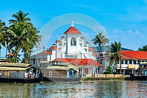 Old colonial Saint Thomas catholic church on the coast of Pamba river, with palms and anchored houseboats, Alleppey, Kerala, South