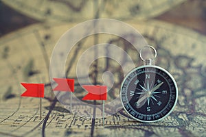 Old compass and flag marking pins on blur vintage map background, journey planning concept