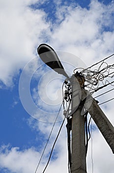 Old concrete electric pole for transmission of wired electricity with lamp post on a background of a cloudy blue sky. Obsolete me