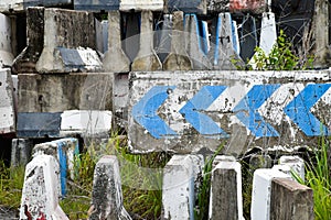 Old concrete road barrier with blue directional arrows is abandoned at a junkyard as a concrete block used to block roads and