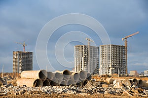 Old concrete sewer pipes for recycling. Salvaging building demolition waste and construction material. Tower cranes working at