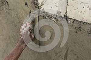 An old construction worker uses a hand trowel to smoothen the concrete surface of a wall. Tropical budget house construction photo