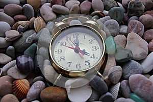 Old copper alarm clock on smooth colored pebbles and seashells