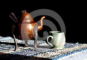 Old copper coffee or tea pot and handmade clay cup at the morning table