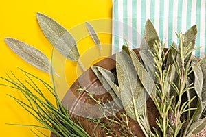 Old copper dish with variety of fresh herbs on blue striped folded towel and yellow background.
