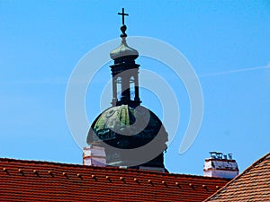 Old copper plated white church clock tower with cross. red clay sloped roofs below