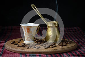 An old copper pot of steaming coffee and a cup of coffee with scattered coffee beans on a tray.