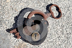 Old corroded padlock with lid and key apart on a granite stone background