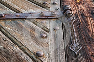 Close-up of an old, corroded and rusty hinge holding the wooden door. Details of wood and metal structure and soft focus