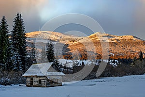 Old cottage under a snowy mountain at sunset