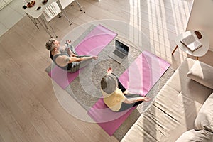 Old couple doing virtual yoga class meditating together at home, top view.