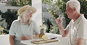 Old couple, laugh and drinking outdoor for fruit snack in garden, diet or retirement. Man, woman and talking in nature