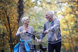 Old couple of pensioners walk with bike in park