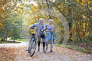 Old couple of pensioners walk with bike in park