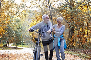 Old couple of pensioners walk with bike in park
