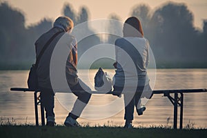 Old couple sitting on a bench by the lakeshore at sunset