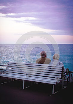 Old couple sitting on a bench looking at calm sea