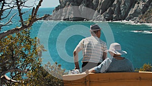 An old couple sitting on a bench and looking at the sea bay