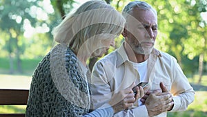 Old couple sitting on bench, man suffering arrhythmia, wife calling emergency