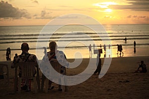 Old couple sitting on chairs enjoying beautiful cloudy sunset at Kuta Beach, Bali, Indonesia