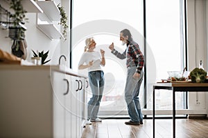 Old couple spends free time dancing twist in modern light kitchen