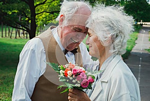 Old couple is walking in the green park. Grandmother and grandfather at golden wedding anniversary celebration. Grandma and