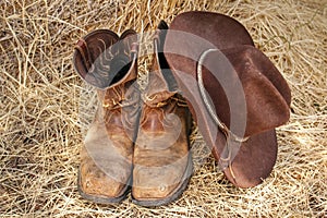 Old cowboy boots and hat on background of hay