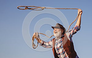 Old cowboy with lasso rope at ranch or rodeo. Bearded western man with brown jacket and hat catching horse or cow.