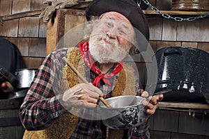 Old cowboy stirs saucepan in outdoor kitchen