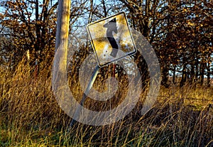 Old and cracked curve ahead sign tilting sideways along a country road in late afternoon with golden sun shinning on it and grass