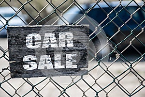 Old cracked rectangular wooden plate on the old green mesh fence with the inscription Car Sale