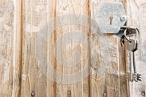 Old, cracked, weathered, wooden door with rusty nails and broken metal face. One iron key is inserted into keyhole and other two