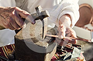 Old craftsman working with hammer on cooper bangle