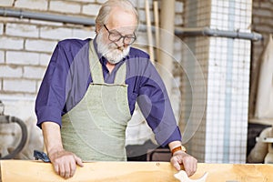 Old craftsperson with shirt and apron holding plank to lay it on the floor of the garage